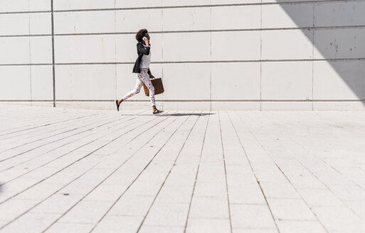 Businesswoman with briefcase running while telephoning with smartphone - UUF007772