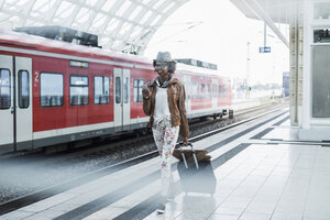 Junge Frau mit Rollkoffer und Smartphone am Bahnsteig - UUF007778