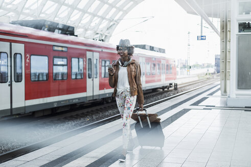 Young woman with trolley bag and smartphone at platform - UUF007778