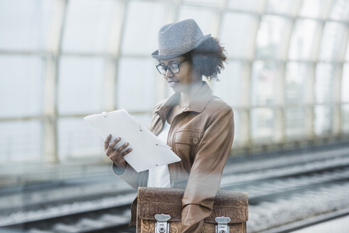 Junge Frau mit Aktentasche und Akte beim Lesen während des Wartens am Bahnsteig - UUF007780