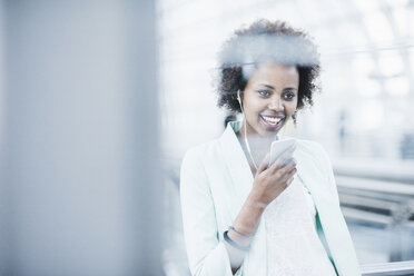 Portrait of smiling young woman with earphones and smartphone at platform - UUF007789