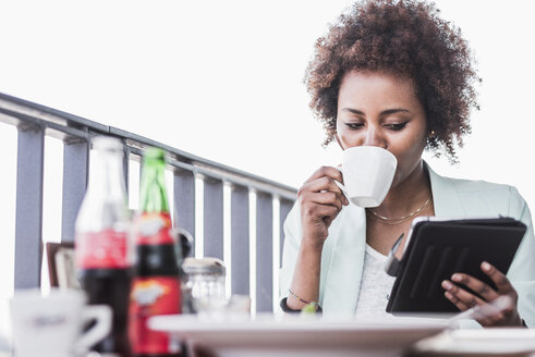 Junge Frau in einem Café, die Kaffee trinkt und auf ihr digitales Tablet schaut - UUF007795