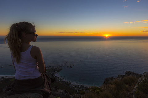 Südafrika, Kapstadt, junges Mädchen genießt den Sonnenuntergang auf dem Kopf eines Berglöwen, lizenzfreies Stockfoto