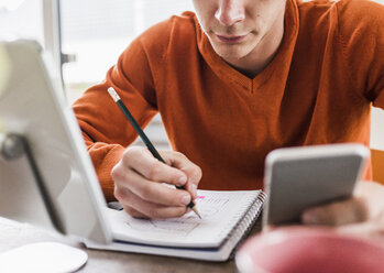 Mann am Schreibtisch mit Mobiltelefon, digitalem Tablet und Notizblock - UUF007812
