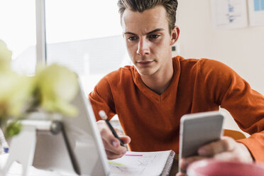 Man at desk with cell phone, digital tablet and notepad - UUF007813