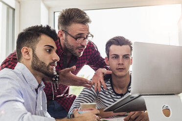 Three young professionals sharing laptop in office - UUF007835