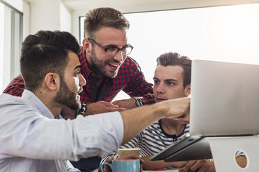 Drei junge Berufstätige teilen sich einen Laptop im Büro - UUF007836