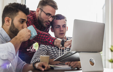 Drei junge Berufstätige teilen sich einen Laptop im Büro - UUF007837