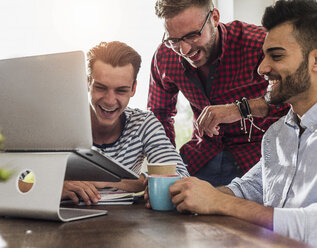Drei glückliche junge Berufstätige teilen sich einen Laptop im Büro - UUF007838