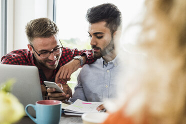 Junge Berufstätige schauen im Büro auf ihr Handy - UUF007846