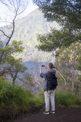 Indonesia, Java, Woman hiking in mountains and taking pictures with smart phone - KNTF000388