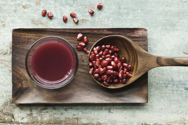 Glass of pomegranate juice and wooden spoon with pomegranate seed on wooden tray - ASF005905