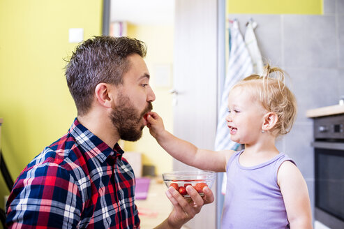 Father and daughter eating tomatoes in kitchen - HAPF000500