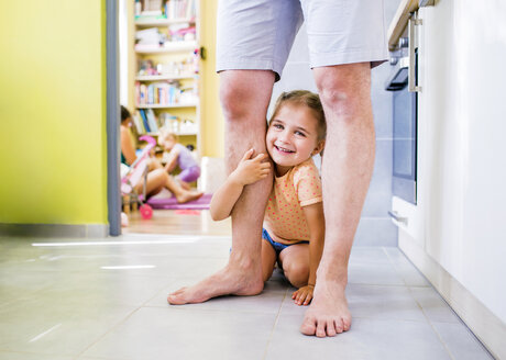 Daughter sitting on floor, holding onto father's leg - HAPF000507