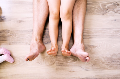 Nackte Beine von Vater und Tochter auf dem Holzboden sitzend - HAPF000516