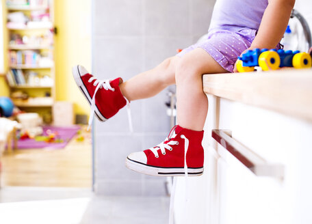 Little girl sitting in kitchen with read canvas shoes - HAPF000518