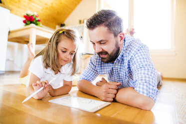 Father and daughter lying on floor, drawing on digital tablet - HAPF000534