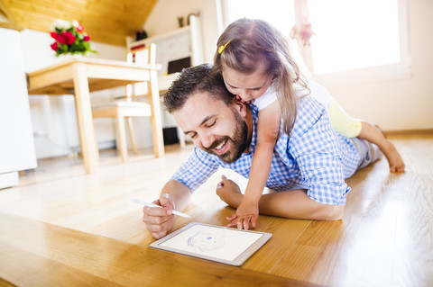 Vater und Tochter liegen auf dem Boden und zeichnen auf einem digitalen Tablet, lizenzfreies Stockfoto