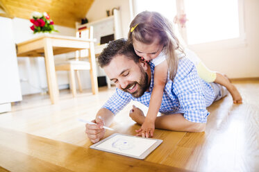 Father and daughter lying on floor, drawing on digital tablet - HAPF000537