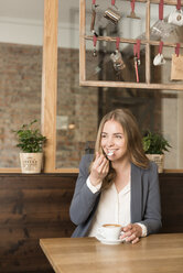 Portrait of smiling young woman tasting cappuccino in a coffee shop - KAF000156