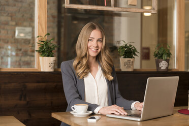 Portrait of smiling young woman using laptop in a coffee shop - KAF000159
