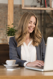 Portrait of smiling young woman using laptop in a coffee shop - KAF000160
