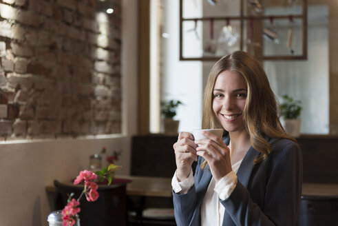 Portrait of smiling young woman drinking coffee in a coffee shop - KAF000163