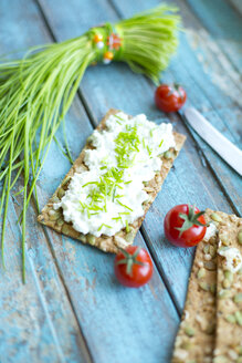 Crispbread, cream cheese, bunch of chive, cocktail tomatos and knife on turquoise wood - MAEF011848