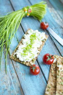 Knäckebrot, Frischkäse, Schnittlauchbündel, Cocktailtomaten und Messer auf türkisfarbenem Holz - MAEF011848