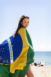 Junge brünette Frau spielt mit brasilianischer Flagge am Strand - VABF000643