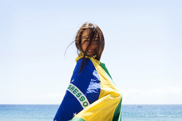 Junge brünette Frau spielt mit brasilianischer Flagge am Strand - VABF000645