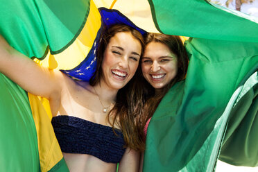 Zwei Freunde in Strandkleidung spielen mit der brasilianischen Flagge - VABF000647