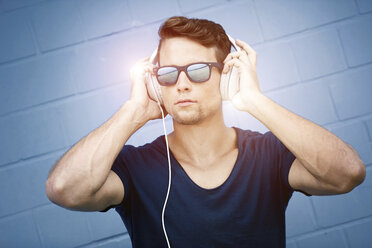 Porträt eines Mannes mit verspiegelter Sonnenbrille, der mit Kopfhörern Musik hört - GDF001036