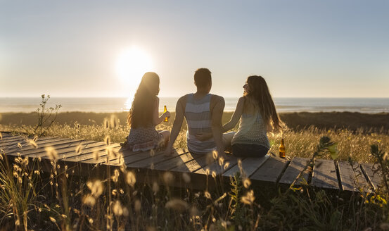 Freunde sitzen auf der Promenade am Strand und trinken Bier bei Sonnenuntergang - MGOF001989