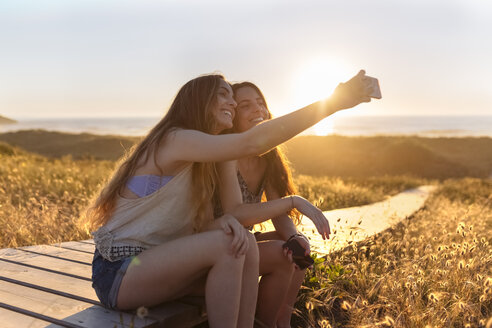 Junge Frauen nehmen Selfie am Strand bei Sonnenuntergang - MGOF001996