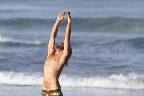 Indonesia, Bali, Young surfer stretching on a beach - KNTF000400