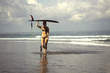 Indonesien, Bali, Frau trägt ihr Surfbrett auf dem Kopf am Strand - KNTF000404