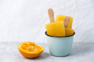 Enamel cup of homemade orange popsicles and a squeezed orange peel - MYF001624