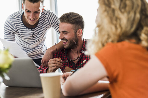 Lächelnde junge Berufstätige teilen sich einen Laptop im Büro - UUF007849