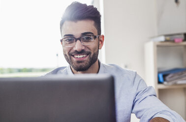 Smiling businessman with laptop in office - UUF007884