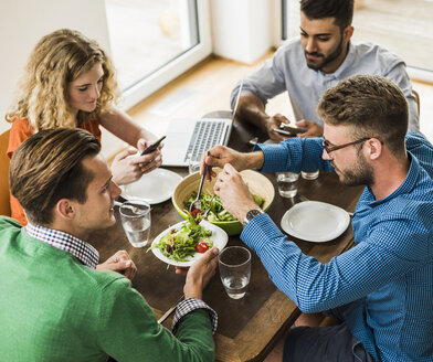 Kollegen am Tisch mit Handy und Laptop beim Mittagessen - UUF007895