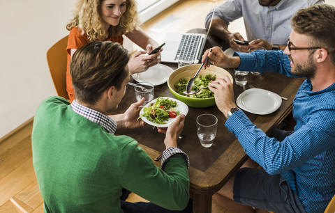 Colleagues at table with cell phone and laptop having lunch stock photo