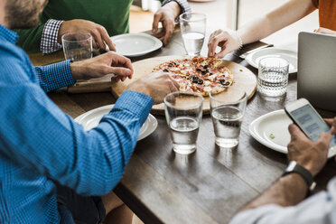 Colleagues at table with cell phone and laptop having a pizza - UUF007897