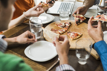 Colleagues at table with cell phone and laptop having a pizza - UUF007900