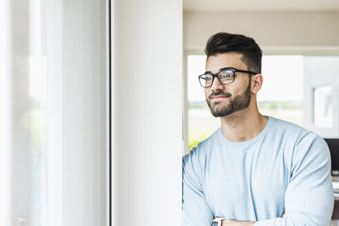 Lächelnder junger Mann schaut aus dem Fenster - UUF007915