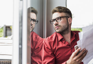 Young man with documents looking out of window - UUF007920