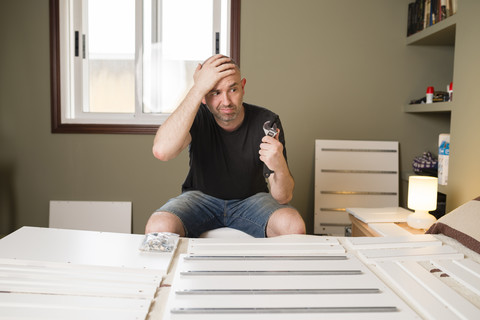 Mann, der zu Hause Möbel zusammenbaut und verzweifelt aussieht, lizenzfreies Stockfoto