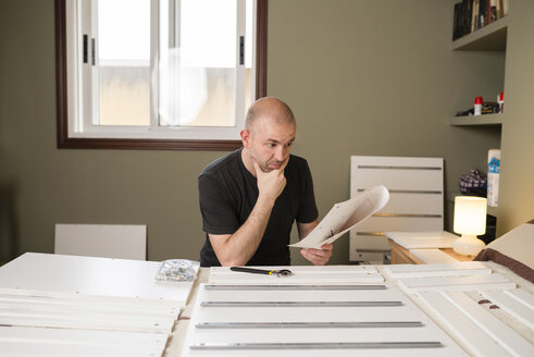 Mann beim Zusammenbau von Möbeln zu Hause, Lesen der Anleitung - RAEF001247