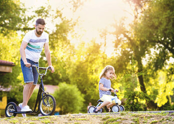Vater und seine kleine Tochter mit Spielzeugauto und Motorroller in einem Park - HAPF000556