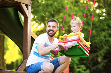 Porträt eines glücklichen Vaters mit seiner kleinen Tochter, die auf einer Schaukel auf dem Spielplatz sitzt - HAPF000559